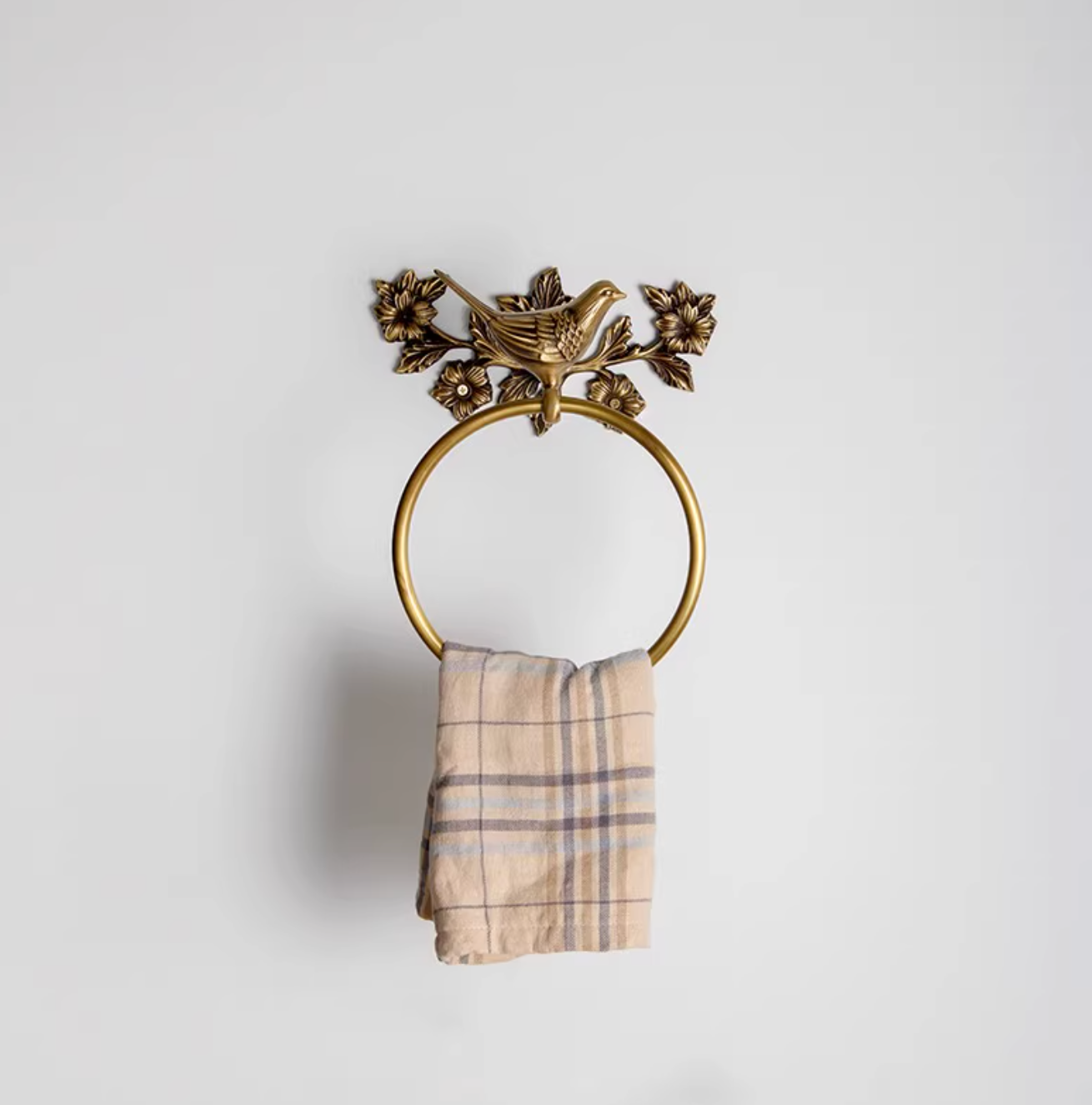 Brass bird towel rack with floral accents and a plaid towel on white background.